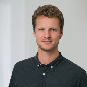 Braune_BAG RelEx Ein Mann mit kurzen Haaren steht vor einem weißen Hintergrund blickt freundlich in die Kamera. Er trägt ein dunkles Hemd.