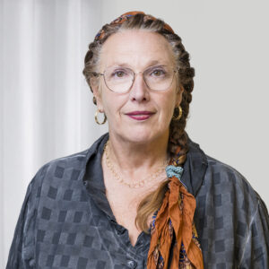 BAG RelEx-938 2 eine Frau langen, zusammengebundenen Haaren steht vor einem weißen Hintergrund und lächelt in die Kamera. Sie trägt ein blaues Oberteil und eine Brille.